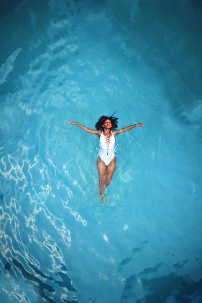 An African American woman in a swimsuit floats peacefully in a clear blue swimming pool thanks to Memorial Pool Services Weekly Pool Cleaning Program