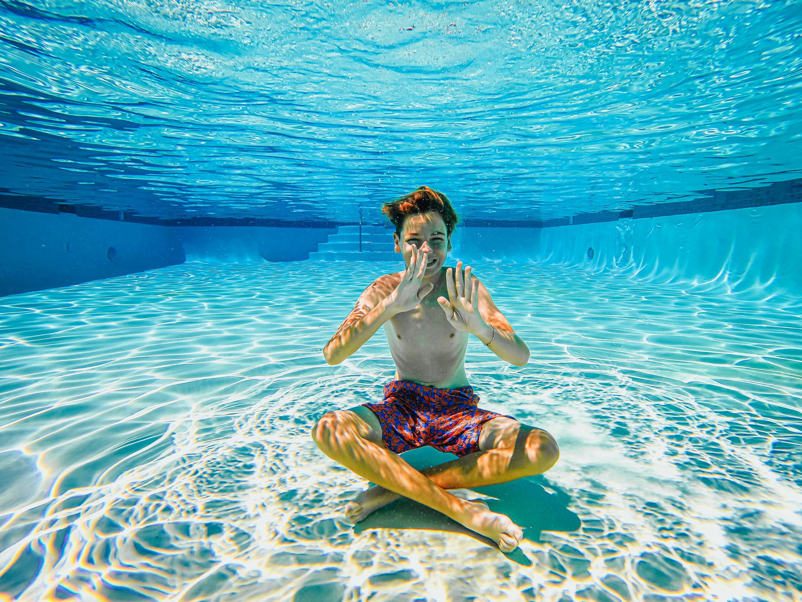 Boy having fun sitting underwater in a sunlit swimming pool.